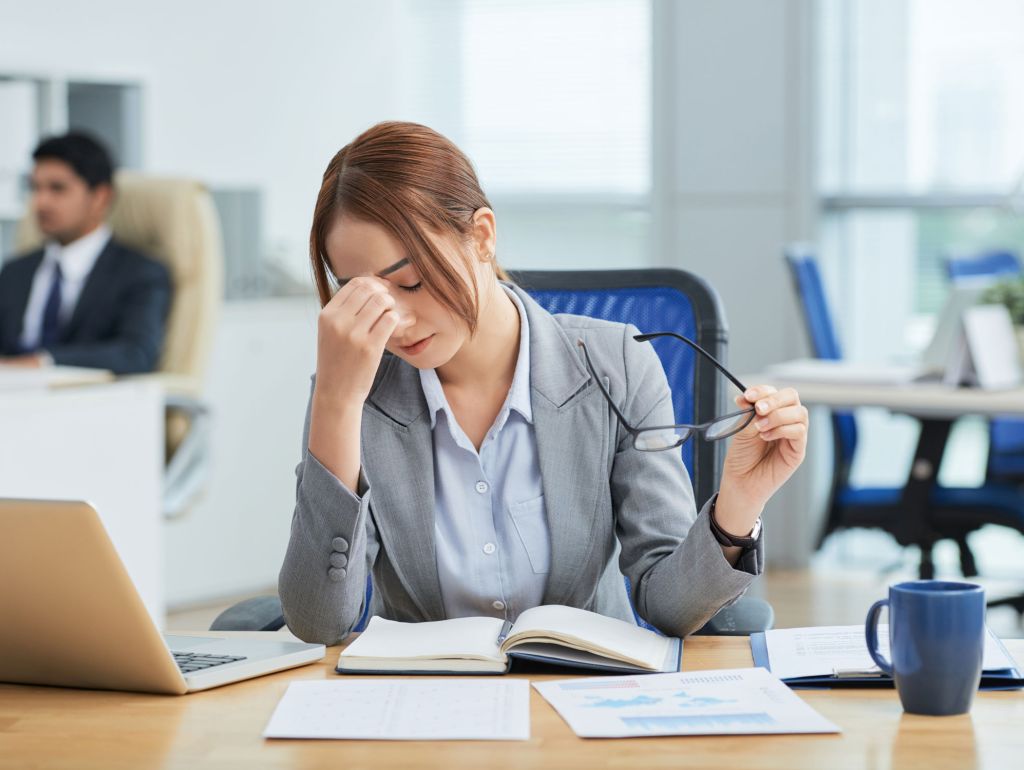 Eine Frau hat Kopfschmerzen am Arbeitsplatz wegen schlechtem Raumklima