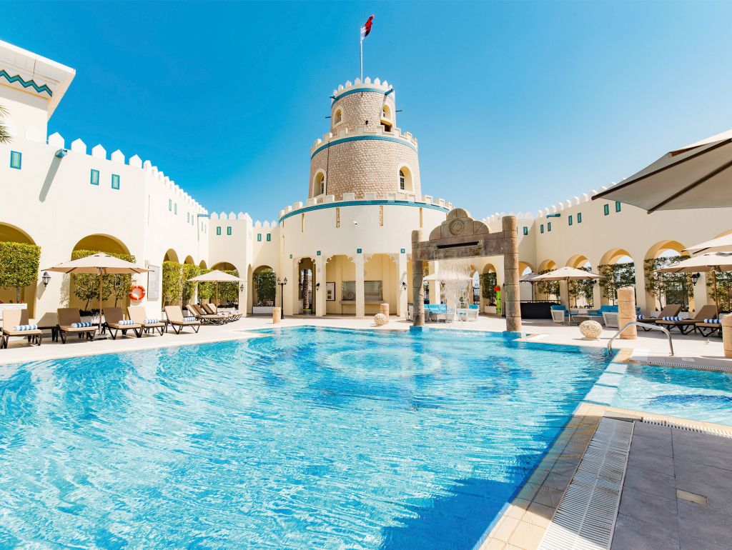 Ein großer Pool mit einem Turm im Hintergrund, gelegen im Diplomatic Club in Doha.