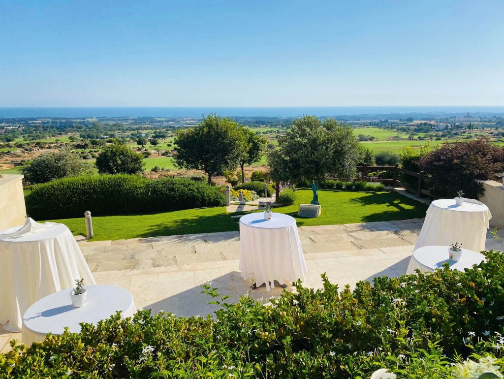 Gedeckte Cocktailtische auf einer Terrasse mit Blick auf den Golfplatz im Eléa Golf Club auf Zypern.