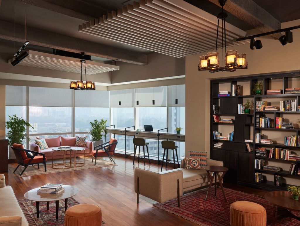 Ein Apartment im The Quorum, Mumbai mit einem Sofa, einem Couchtisch, einem Bücherregal und einem Fenster mit Ausblick zur Stadt.